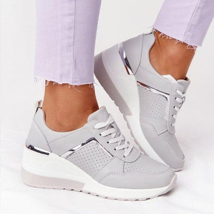 Graue Damen-Sneaker mit Keilabsatz, silbernen Details und perforiertem Design. Modische Freizeitschuhe, ideal für trendige Outfits.
