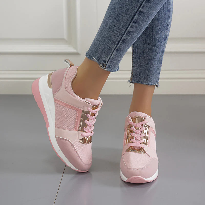 Frau trägt rosa Sneaker mit weißer Sohle und goldenen Details, kombiniert mit blauen Jeans. Modische Damenschuhe, bequem und stilvoll.