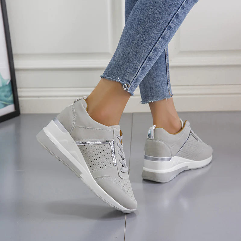 Damen Sneaker in Grau mit Keilabsatz, silbernen Details und perforiertem Design. Modische Freizeitschuhe, ideal für den Alltag.