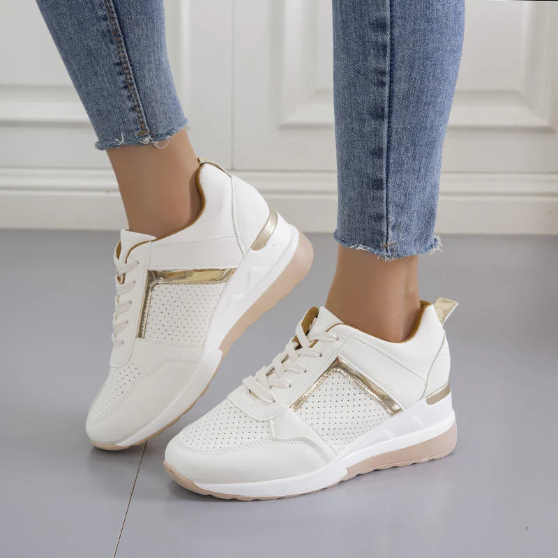 Damen-Sneaker in Weiß mit goldenen Akzenten, perforiertem Design und dicker Sohle, getragen mit blauen Jeans. Modische Freizeitschuhe für Damen.