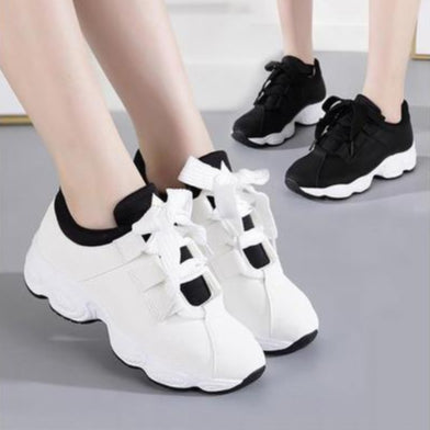 Zwei Paar modische Sneaker, weiß und schwarz, mit dicker Sohle und Schleifen, auf grauem Boden. Trendige Sportschuhe für Damen.