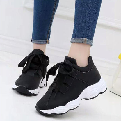 Schwarze Sneaker mit dicker weißer Sohle, getragen von Person in blauen Jeans. Modische Sportschuhe, ideal für Freizeit und Sport.