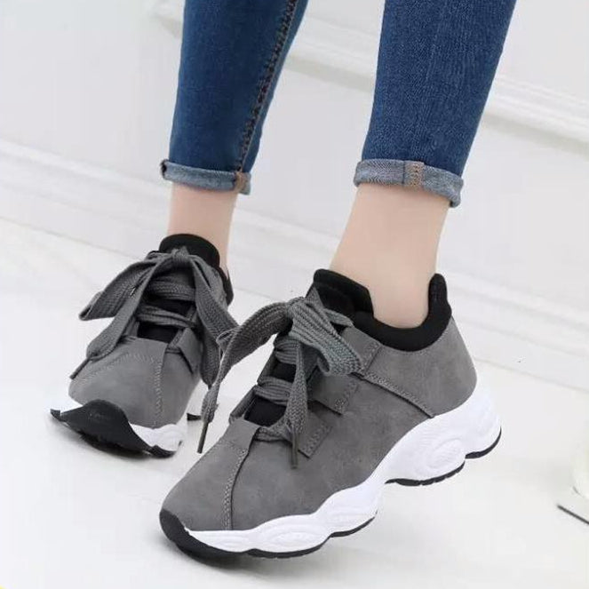 Graue Damen-Sneaker mit dicker weißer Sohle und breiten Schnürsenkeln, getragen mit blauen Jeans. Modische Freizeitschuhe für Damen.