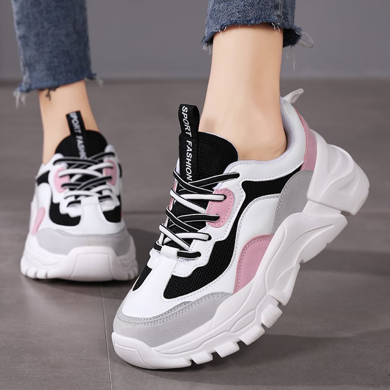 Damen-Sneaker in Weiß, Schwarz und Rosa mit dicker Sohle und Schnürsenkeln, getragen zu blauen Jeans. Modische Sportschuhe für Freizeit und Sport.