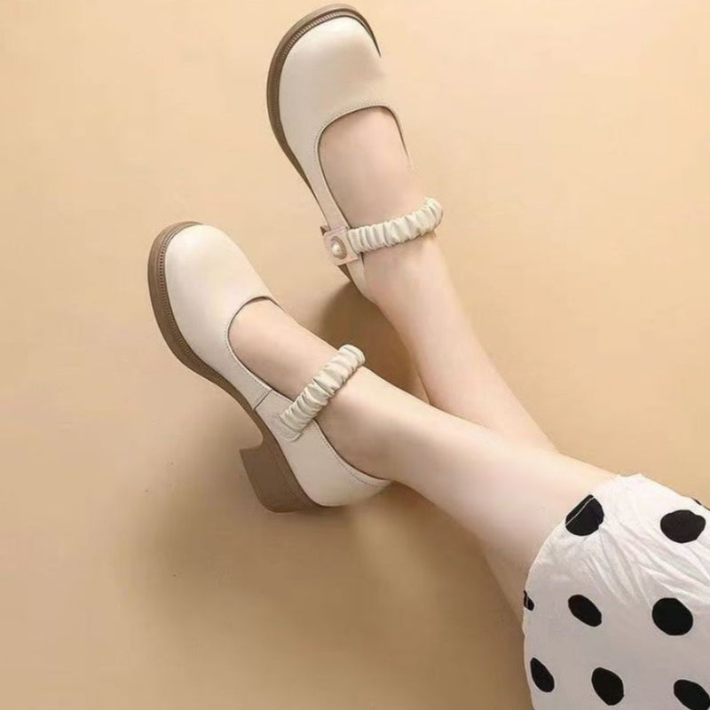 Beige Mary Jane Schuhe mit Blockabsatz und elastischem Riemen, getragen von einer Person in einem weißen Rock mit schwarzen Punkten.
