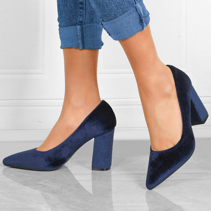 Damenfüße in blauen Samt-High-Heels, kombiniert mit hochgekrempelten Jeans. Elegante, modische Schuhe, ideal für stilvolle Anlässe.