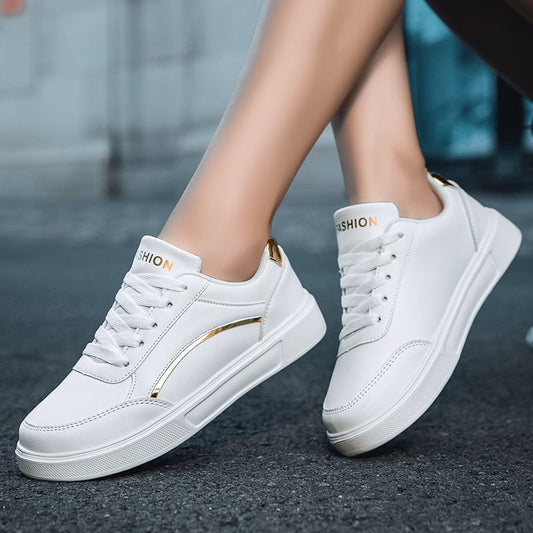 Weiße Damen-Sneaker mit goldenen Akzenten, modisch und bequem, auf Asphalt getragen. Ideal für Freizeit und Streetstyle.