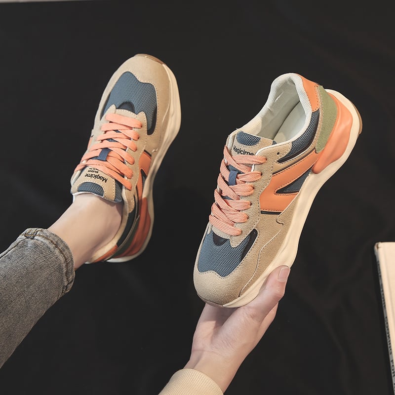 Person hält modische Sneaker in Beige, Blau und Orange mit dicker Sohle. Trendige Sportschuhe, bequeme Freizeitschuhe, stilvolle Turnschuhe.