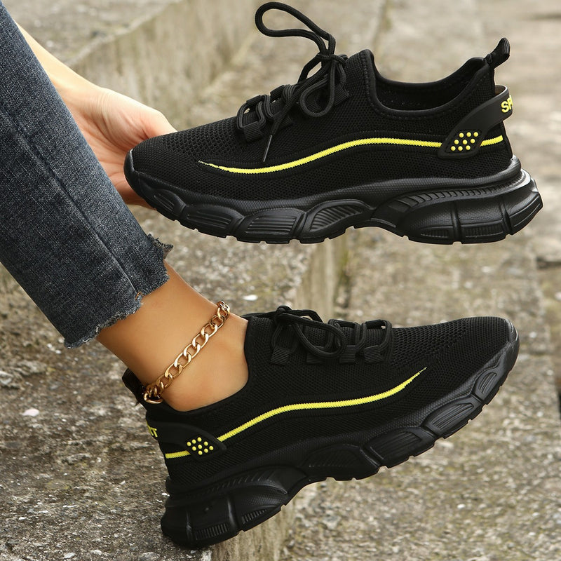 Schwarze Sneaker mit gelben Akzenten, atmungsaktives Mesh, dicke Sohle, sportlich, modern, Damenmode, Straßenstil, Nahaufnahme.