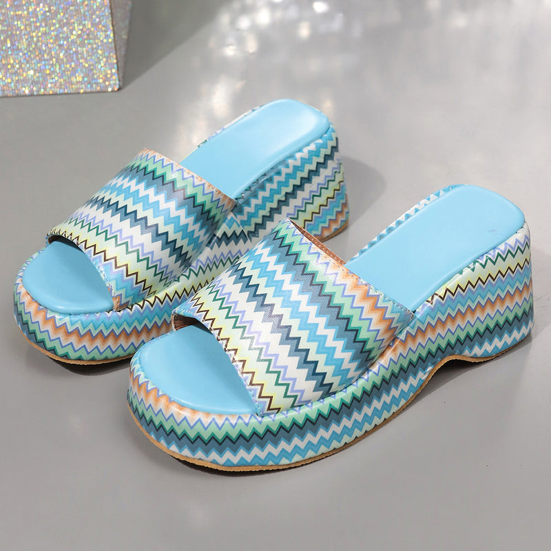 Bunte Plateau-Sandalen mit Zickzackmuster, blauem Fußbett und offenem Zehenbereich auf grauem Hintergrund. Modische Damenschuhe, Sommertrend.