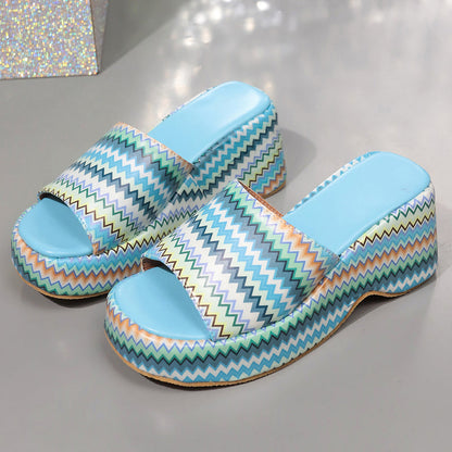 Bunte Plateau-Sandalen mit Zickzackmuster, blauem Fußbett und offenem Zehenbereich auf grauem Hintergrund. Modische Damenschuhe, Sommertrend.