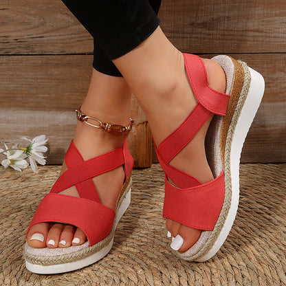 Rote Damen-Sandalen mit Keilabsatz, Kreuzriemen und geflochtener Sohle, getragen auf Holzboden. Sommermode, bequeme Schuhe, trendige Sandalen.