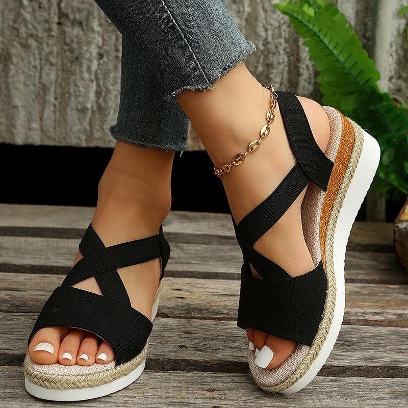 Schwarze Sandalen mit Keilabsatz und geflochtener Sohle, getragen von einer Person mit Jeans. Modische Sommerschuhe, ideal für Damen.