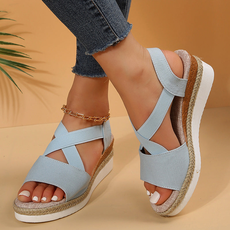 Damen-Sandalen mit Keilabsatz in Hellblau, Kreuzriemen-Design, Jeans kombiniert, goldene Fußkette, Sommermode, beiger Hintergrund.