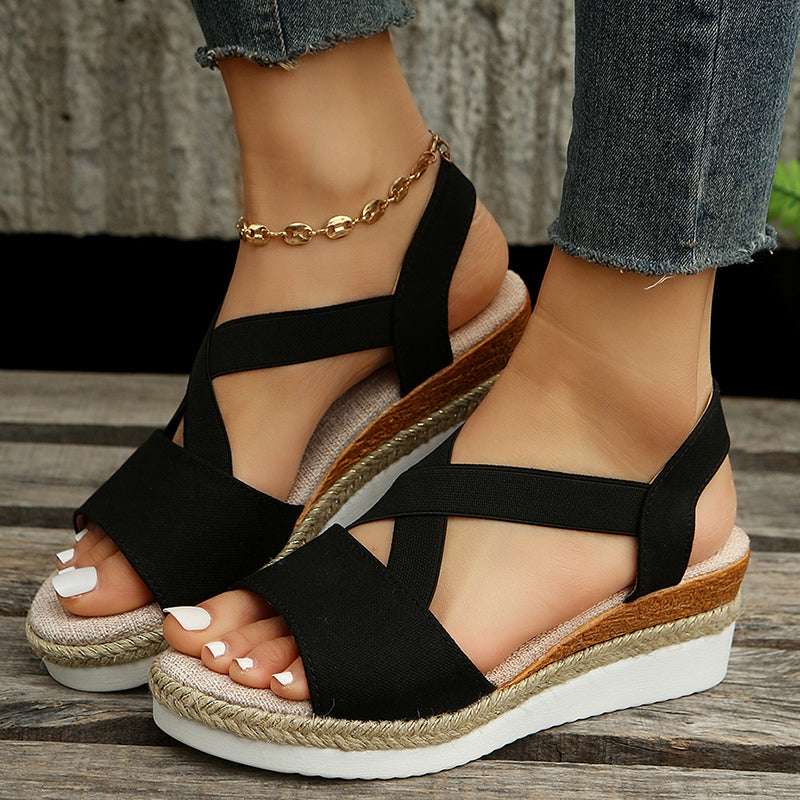 Schwarze Damen-Sandalen mit Keilabsatz und Bastsohle, getragen mit Jeans. Modische Sommerschuhe, ideal für Freizeit und Strand.