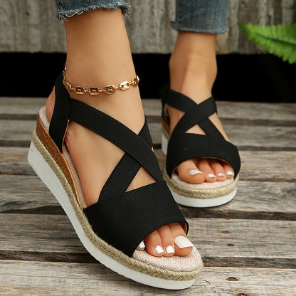Schwarze Damen-Sandalen mit Keilabsatz und Kreuzriemen, getragen mit Jeans. Modische Sommerschuhe, ideal für Freizeit und Strand.