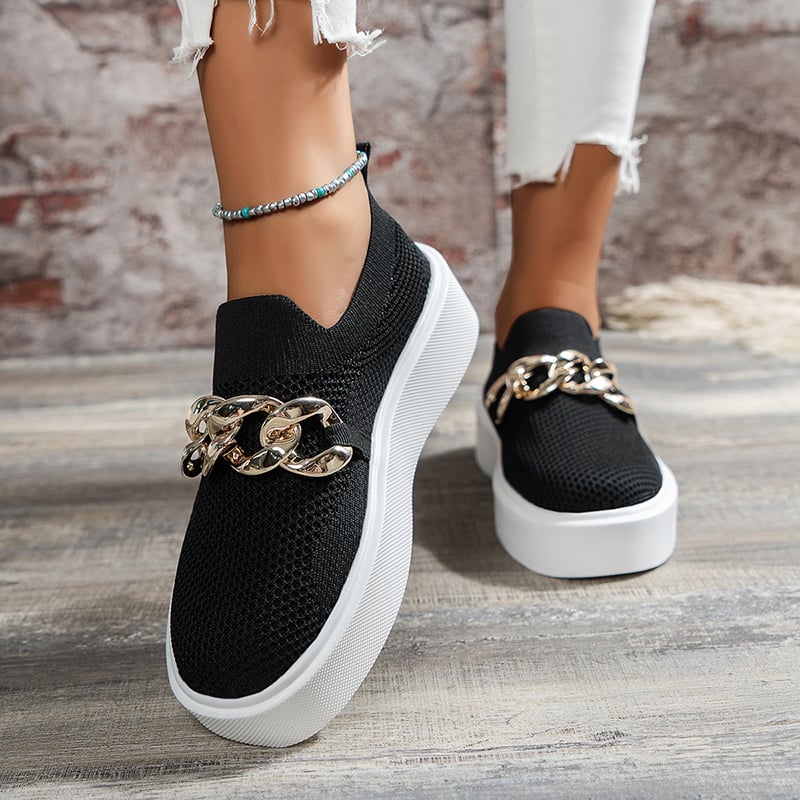 Schwarze Damen-Sneaker mit goldener Kette, weiße Sohle, getragen mit weißer Jeans und türkisfarbenem Fußkettchen, modisch, urbaner Stil.