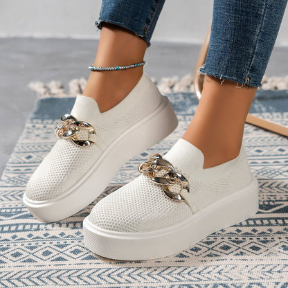 Weiße Damen-Sneaker mit Plateau, Strickmuster und goldener Kettendekoration, getragen auf blauem Teppich. Modische Freizeitschuhe für Damen.