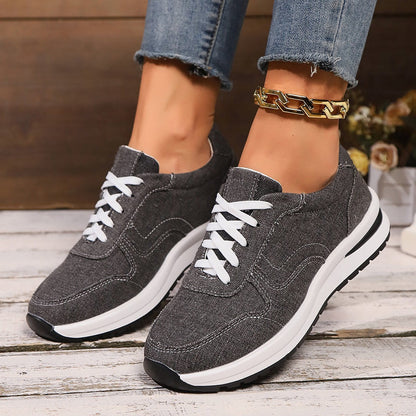 Graue Damen-Sneaker mit weißer Sohle und Schnürsenkeln, getragen mit blauer Jeans. Modische Freizeitschuhe, ideal für Alltag und Sport.