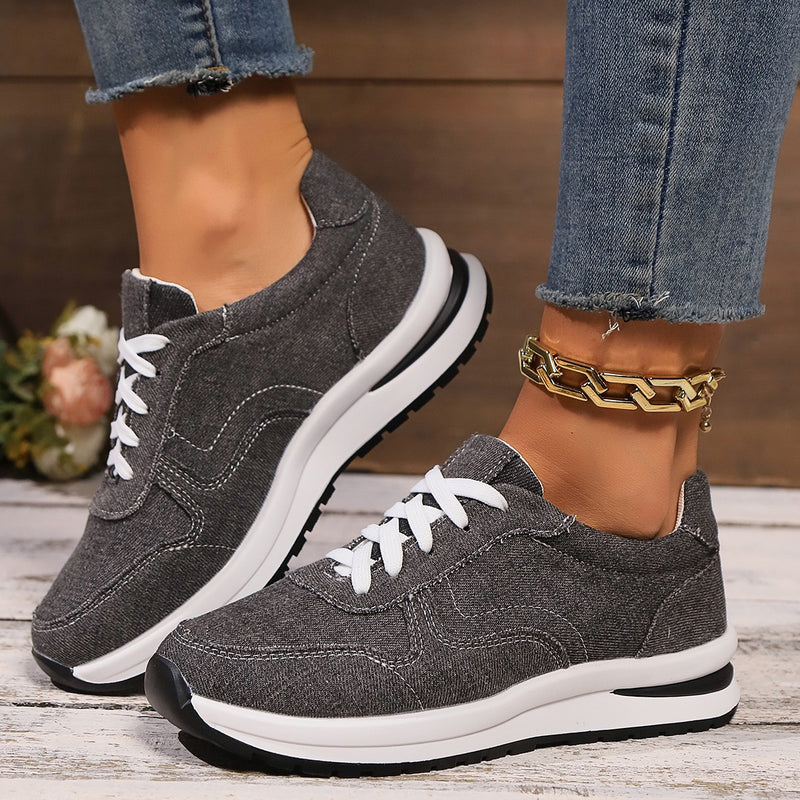 Graue Damen-Sneaker mit weißer Sohle und Schnürsenkeln, getragen mit blauer Jeans. Modische Freizeitschuhe, ideal für Alltag und Sport.