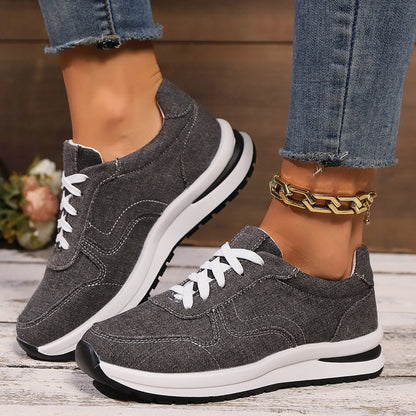 Graue Damen-Sneaker mit weißer Sohle und Schnürsenkeln, getragen mit blauer Jeans. Modische Freizeitschuhe, ideal für Alltag und Sport.
