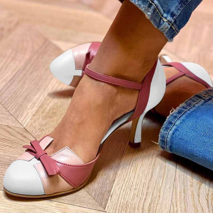 Damenfüße in rosa-weißen High Heels mit Schleifen, auf Holzfußboden. Modische Schuhe, elegantes Design, ideal für stilvolle Anlässe.