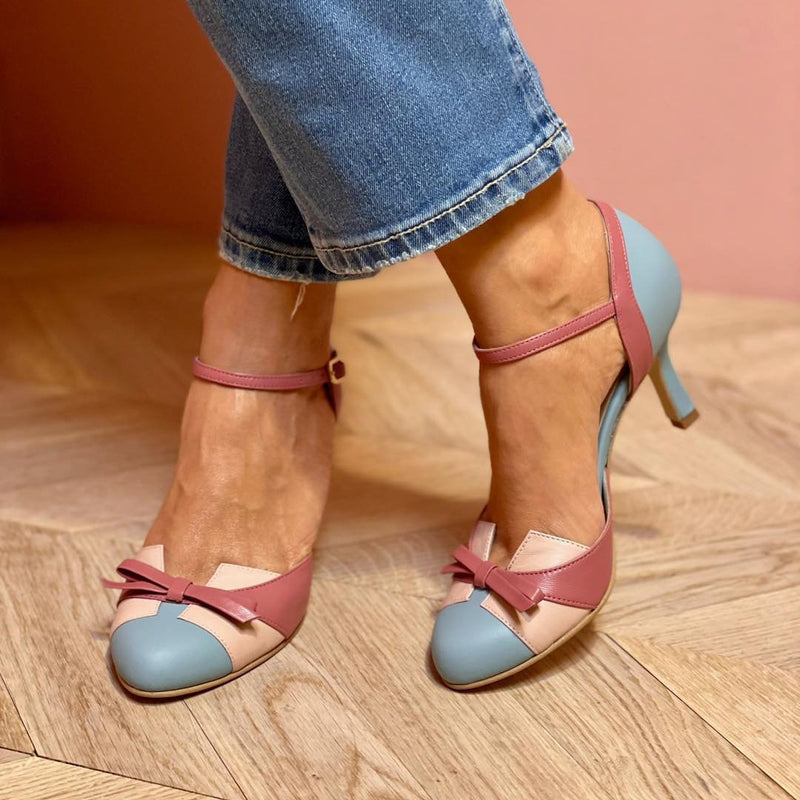 Frau trägt elegante, mehrfarbige High Heels mit Schleifen-Detail, kombiniert mit blauen Jeans. Modische Damenschuhe, stilvoller Look.