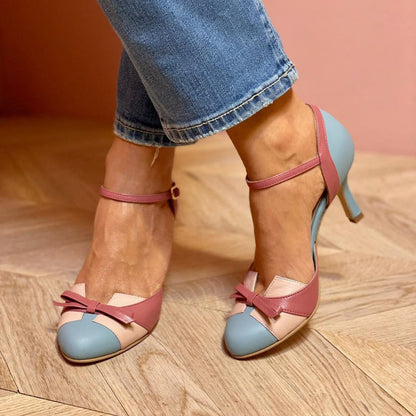 Frau trägt elegante, mehrfarbige High Heels mit Schleifen-Detail, kombiniert mit blauen Jeans. Modische Damenschuhe, stilvoller Look.