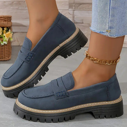 Damen-Loafer in Dunkelblau mit dicker Sohle, kombiniert mit Jeans und goldener Fußkette. Modische Schuhe für Herbst und Winter.