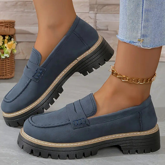 Damen-Loafer in Dunkelblau mit dicker Sohle, kombiniert mit Jeans und goldener Fußkette. Modische Schuhe für Herbst und Winter.