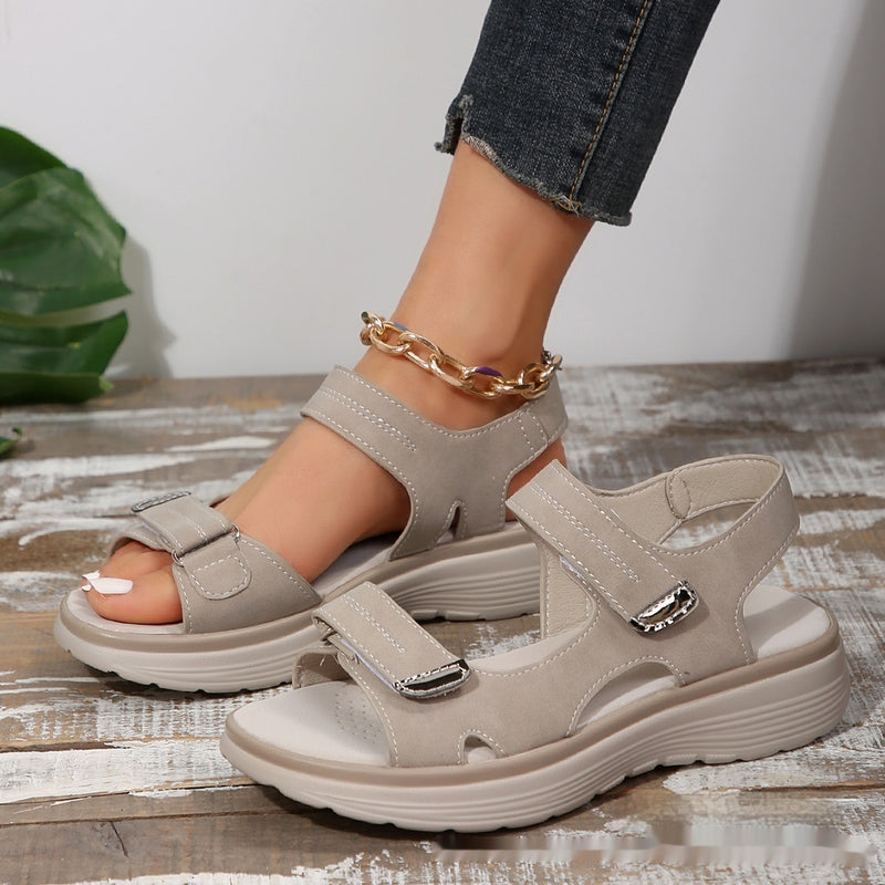 Damen Sandalen mit Klettverschluss, beige, auf Holzfußboden. Bequeme Sommerschuhe, modisch, ideal für Freizeit und Outdoor-Aktivitäten.