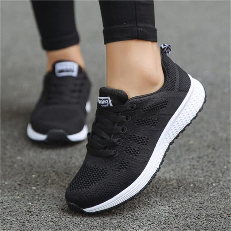 Schwarze Damen-Sneaker mit weißer Sohle, atmungsaktives Mesh-Design, ideal für Laufen und Freizeit, auf Asphalt getragen.