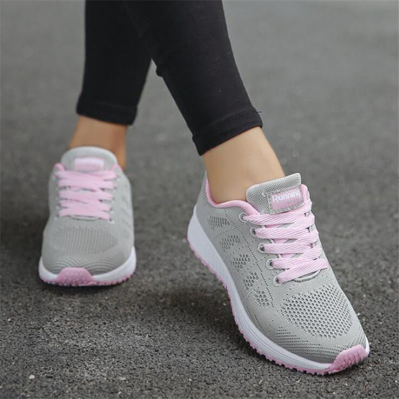 Graue Damen-Laufschuhe mit rosa Schnürsenkeln auf Asphalt. Bequeme Sportschuhe für Fitness und Jogging. Ideal für Outdoor-Aktivitäten.