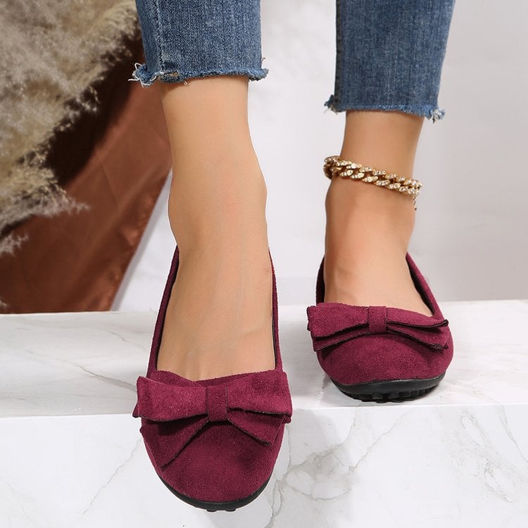 Damenfüße in weinroten Ballerinas mit Schleife, kombiniert mit blauen Jeans. Modische Schuhe, elegantes Design, ideal für Freizeit und Büro.