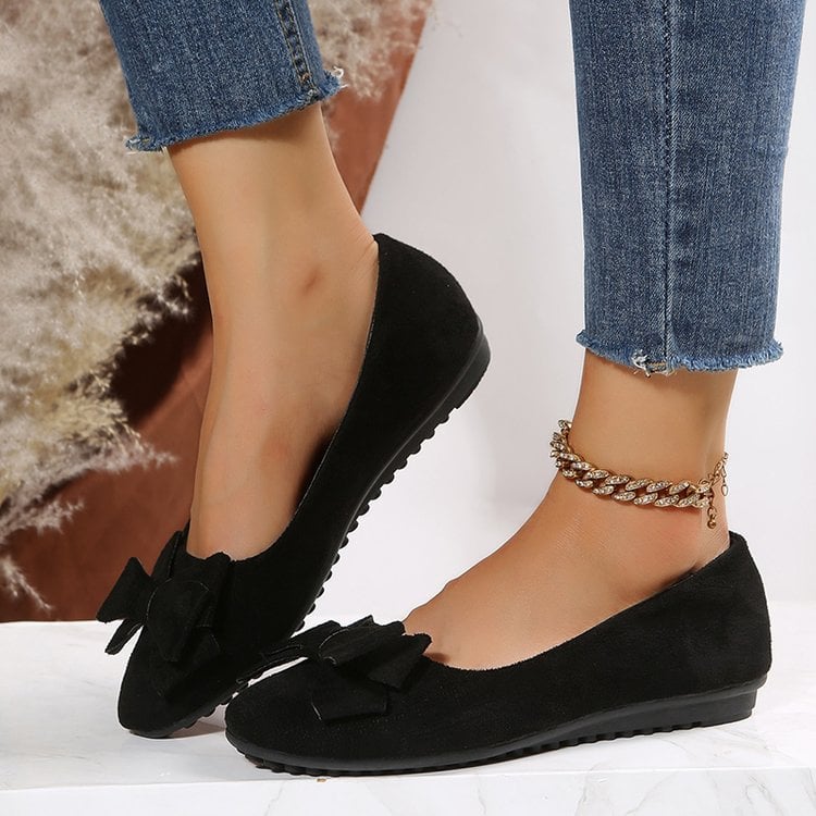 Schwarze Damen-Ballerinas mit Schleife, getragen mit blauen Jeans. Modische, bequeme Schuhe für Alltag und Freizeit. Elegante Fußkettchen als Accessoire.