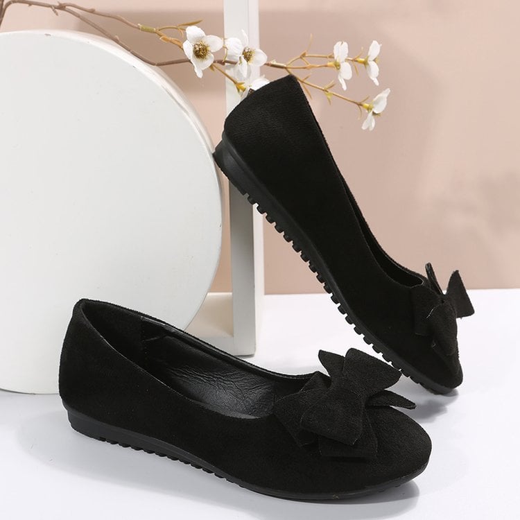 Schwarze Damen-Ballerinas mit Schleife, flache Sohle, elegantes Design, ideal für Freizeit und Büro, vor weißem Hintergrund mit Blumen.