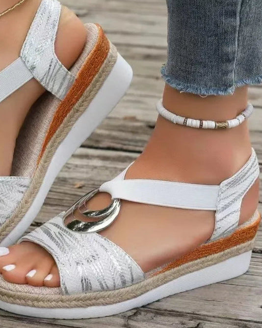 Damen-Sandalen mit Keilabsatz, weißem Stoff, silbernem Ringdetail, kombiniert mit Jeans und Fußkettchen auf Holzuntergrund.