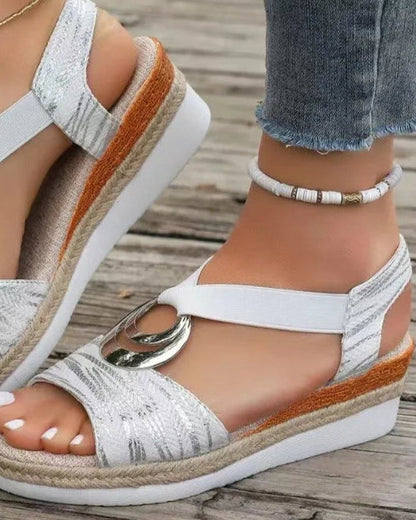 Damen-Sandalen mit Keilabsatz, weißem Stoff, silbernem Ringdetail, kombiniert mit Jeans und Fußkettchen auf Holzuntergrund.