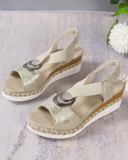 Beige Sandaletten mit Keilabsatz, Schlangenleder-Optik und elastischen Riemen auf hellem Hintergrund. Modische Damenschuhe für Sommer.