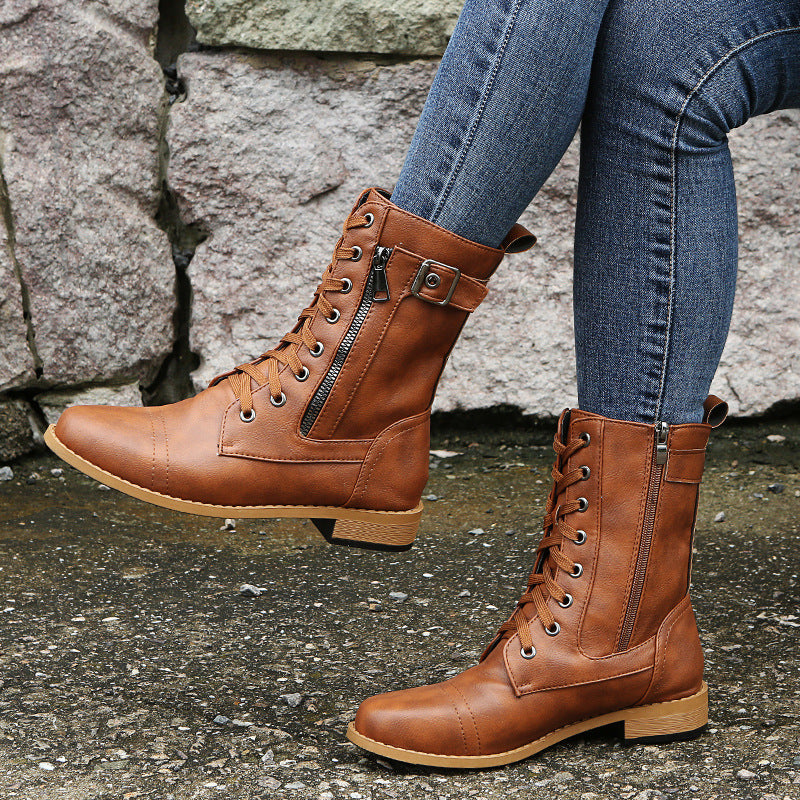 Braune Damen-Schnürstiefel aus Leder mit Reißverschluss, getragen zu blauen Jeans, vor einer Steinmauer. Modische Herbst- und Winterstiefel.