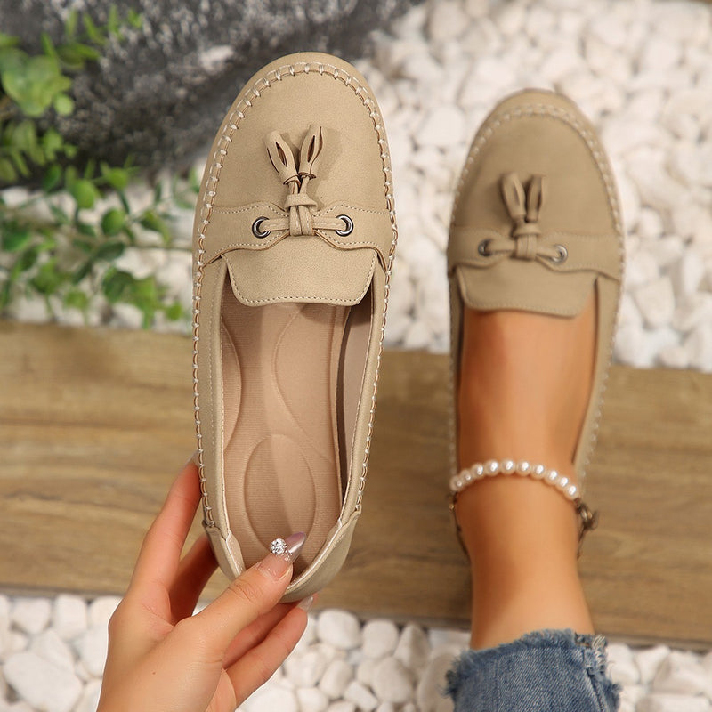 Beige Mokassins mit Quasten, getragen von einer Person auf Kieselsteinen. Modische Damen-Schuhe, ideal für Freizeit und Sommer.