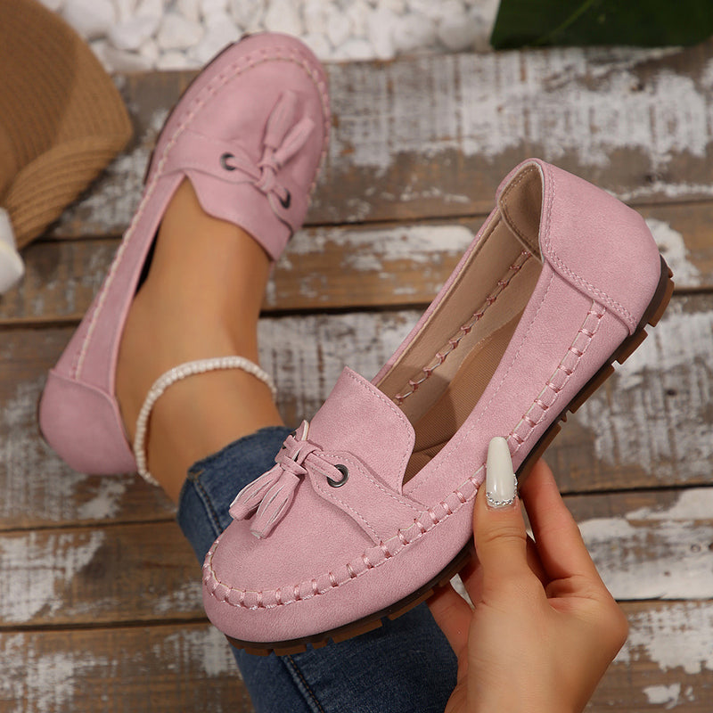 Rosa Mokassins für Damen, aus Wildleder, mit Quasten, auf Holzuntergrund. Modische, bequeme Schuhe, ideal für Freizeit und Alltag.