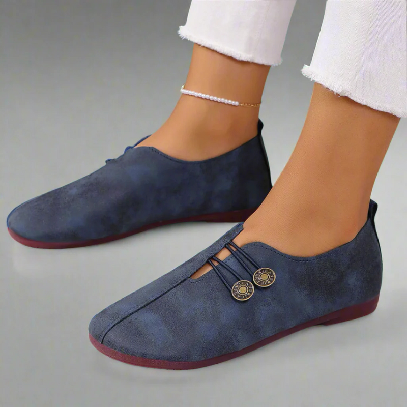 Damen blaue Wildleder-Slipper mit Knopfdetails, kombiniert mit weißen Jeans. Bequeme, stilvolle Freizeitschuhe für den Alltag.