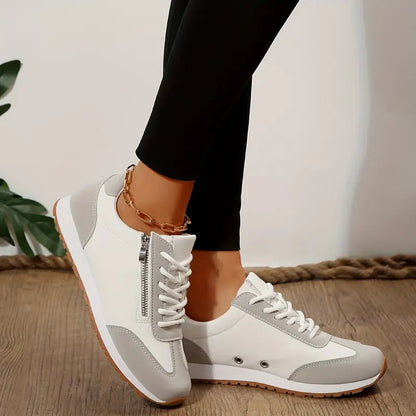 Damen-Sneaker in Weiß und Grau mit Reißverschluss, getragen von Person in schwarzer Leggings, auf Holzboden. Modische Freizeitschuhe.