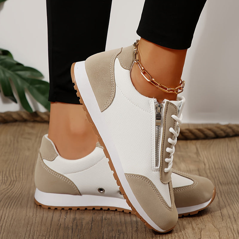 Damen-Sneaker in Beige und Weiß mit Reißverschluss, getragen von Person mit schwarzer Hose und goldener Fußkette, auf Holzboden.