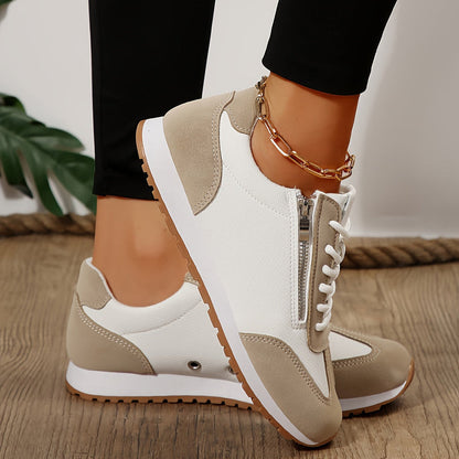 Damen-Sneaker in Beige und Weiß mit Reißverschluss, getragen von Person mit schwarzer Hose und goldener Fußkette, auf Holzboden.