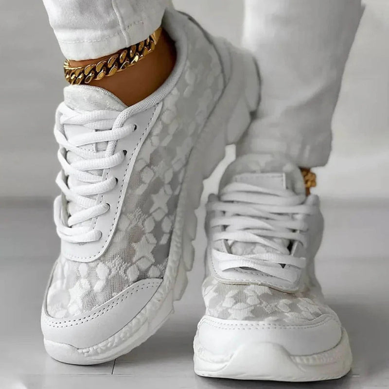 Weiße Damen-Sneaker mit Spitzenmuster, goldene Knöchelketten, modische Schuhe, Freizeitlook, stilvolle Damenmode, Nahaufnahme.