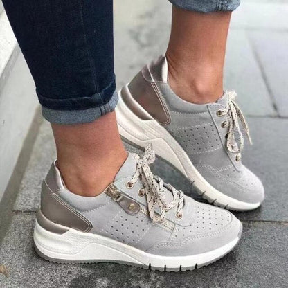 Graue Damen-Sneaker mit weißer Sohle und Schnürsenkeln, getragen von Person in Jeans. Modische Freizeitschuhe, ideal für Alltag und Sport.