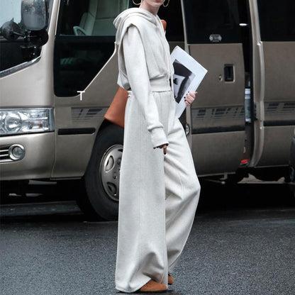 Frau in elegantem, cremefarbenem Jumpsuit mit Kapuze, hält Magazin, steht vor silbernem Van. Modetrend, Streetstyle, urbaner Look.