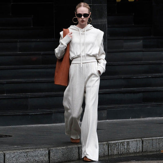 Frau in weißem Hoodie und weiten Hosen, trägt braune Tasche, Sonnenbrille und Ohrringe. Modetrend, urbaner Stil, Streetwear, Herbstmode.
